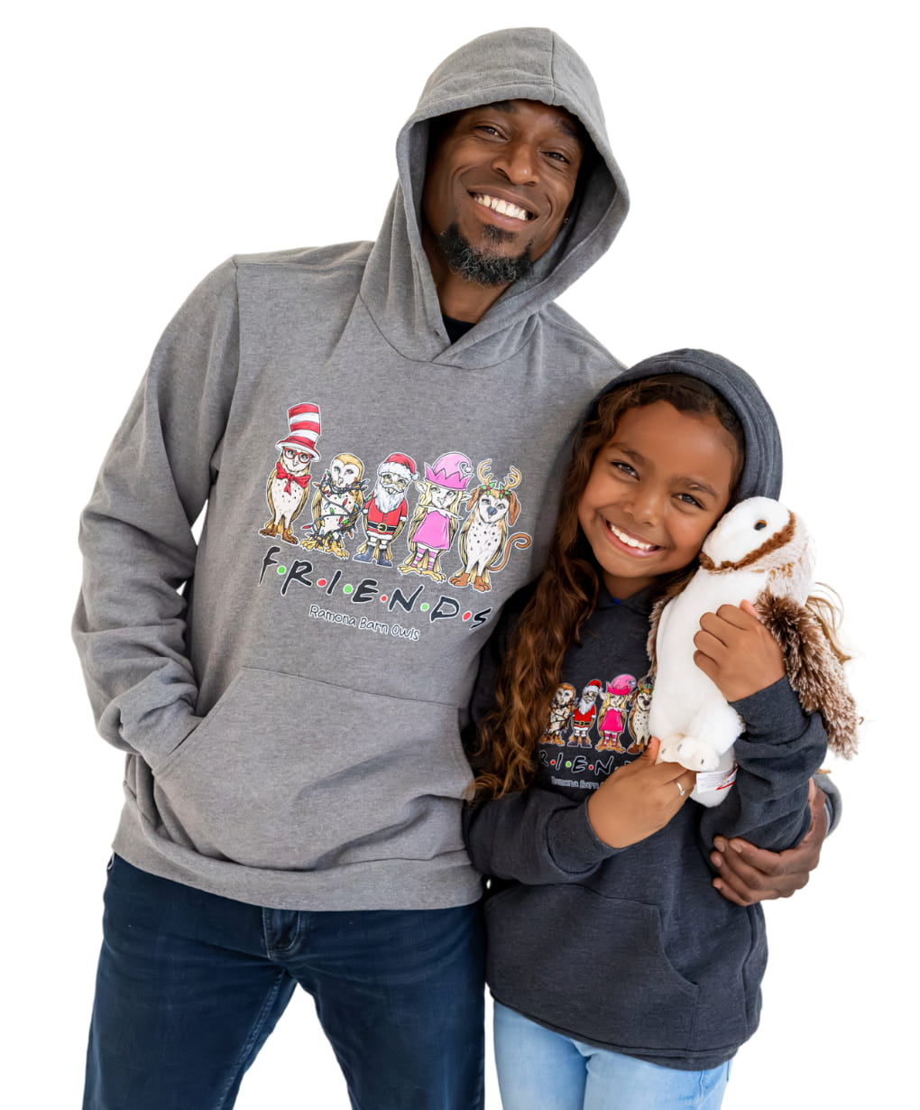 Dad and daughter standing together in matching hoodies, daughter hugging owl plushie.